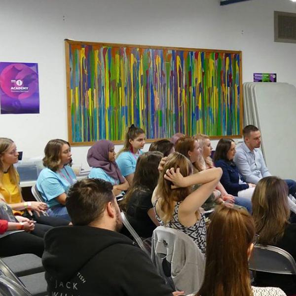 Young people sitting on chairs listening to someone speak